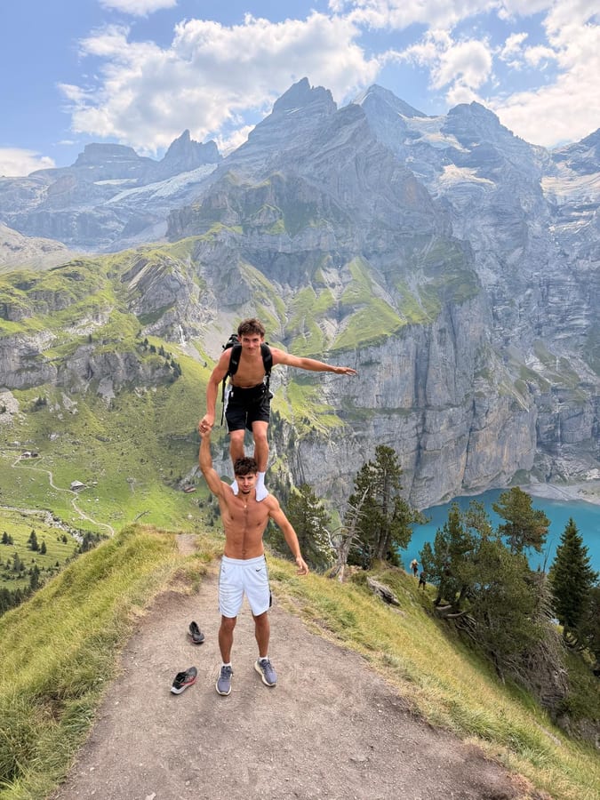 Un ami porté sur les épaules de l'autre, bras écartés, face à un lac de montagne en Suisse.