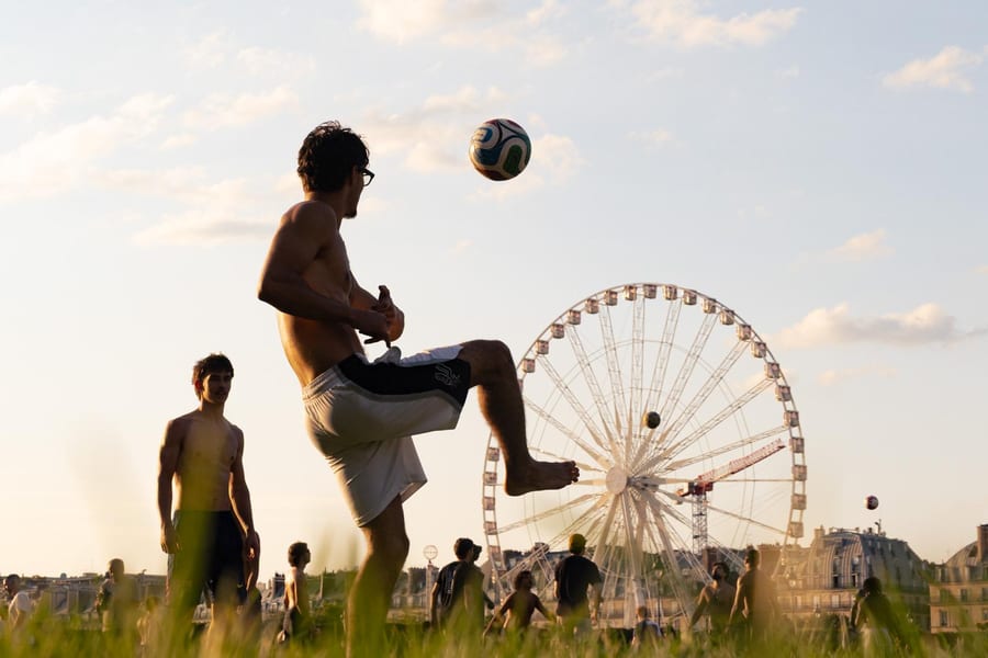 Un joueur jongle avec un ballon en plein air à Paris, grande roue en arrière-plan.