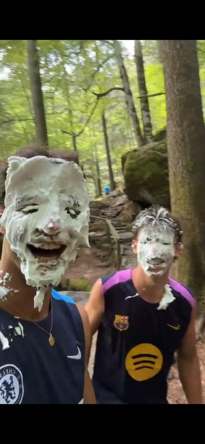 Deux amis chahutent, visages couverts de mousse à raser, en pleine forêt.