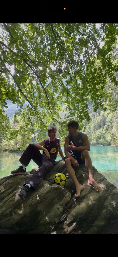 Les deux amis assis sur un rocher au bord d'un lac turquoise, ballon à leurs pieds.